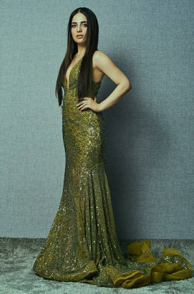 Radhika  in a gold-toned sequined gown with deep plunge and a train