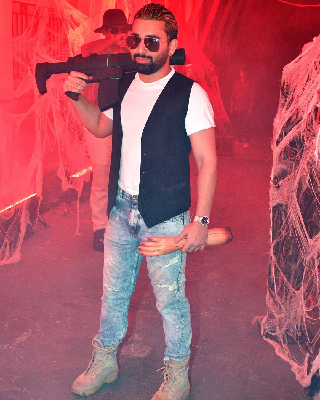 Halloween Party Host Orhan Awatramani  In A White Tee Half Jacket, Denim, And A Big Gun In One Hand