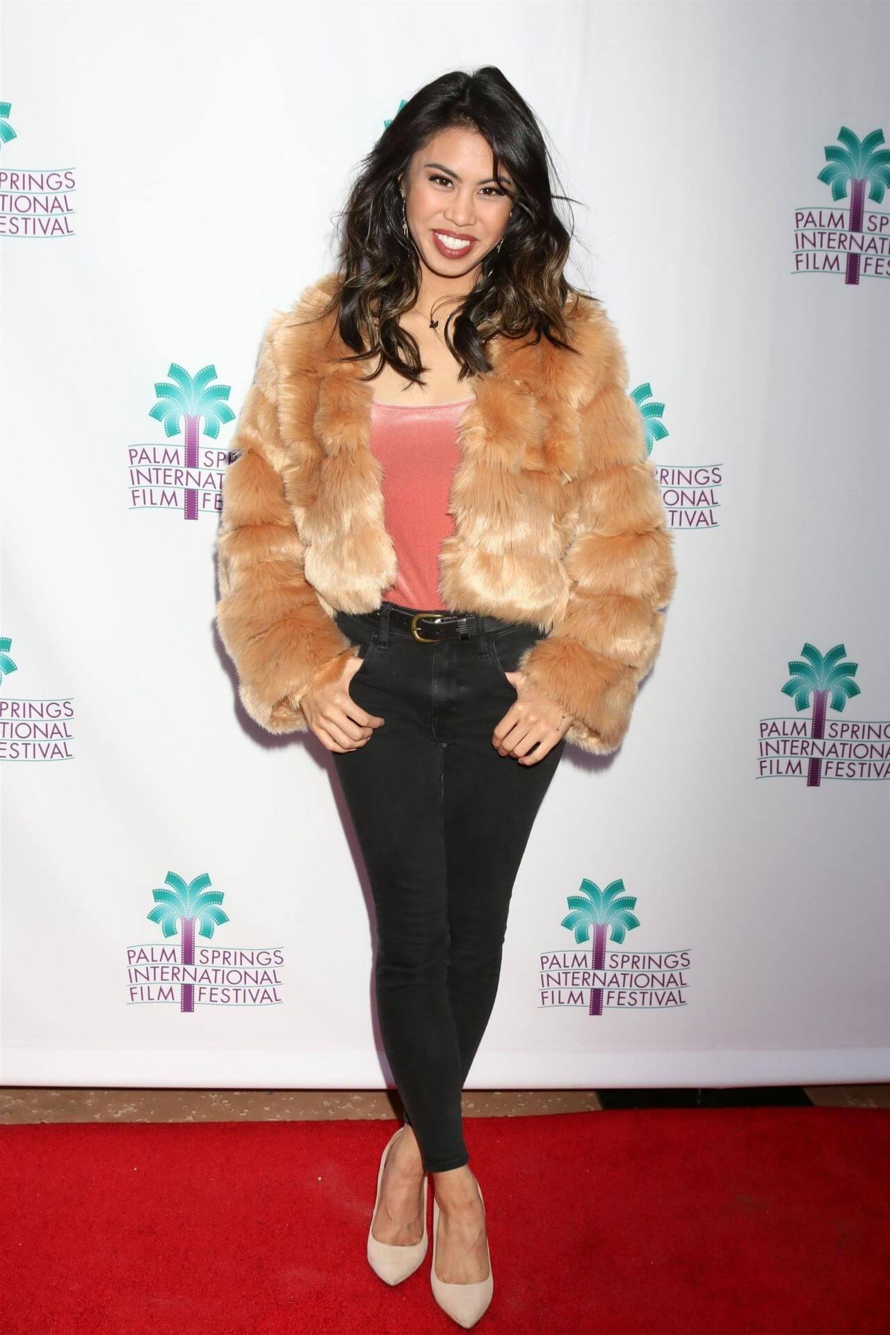 Ashley Argota In Orange Top & Black Jeans With Fur Coat At Palm Springs International Film Festival in Palm Springs