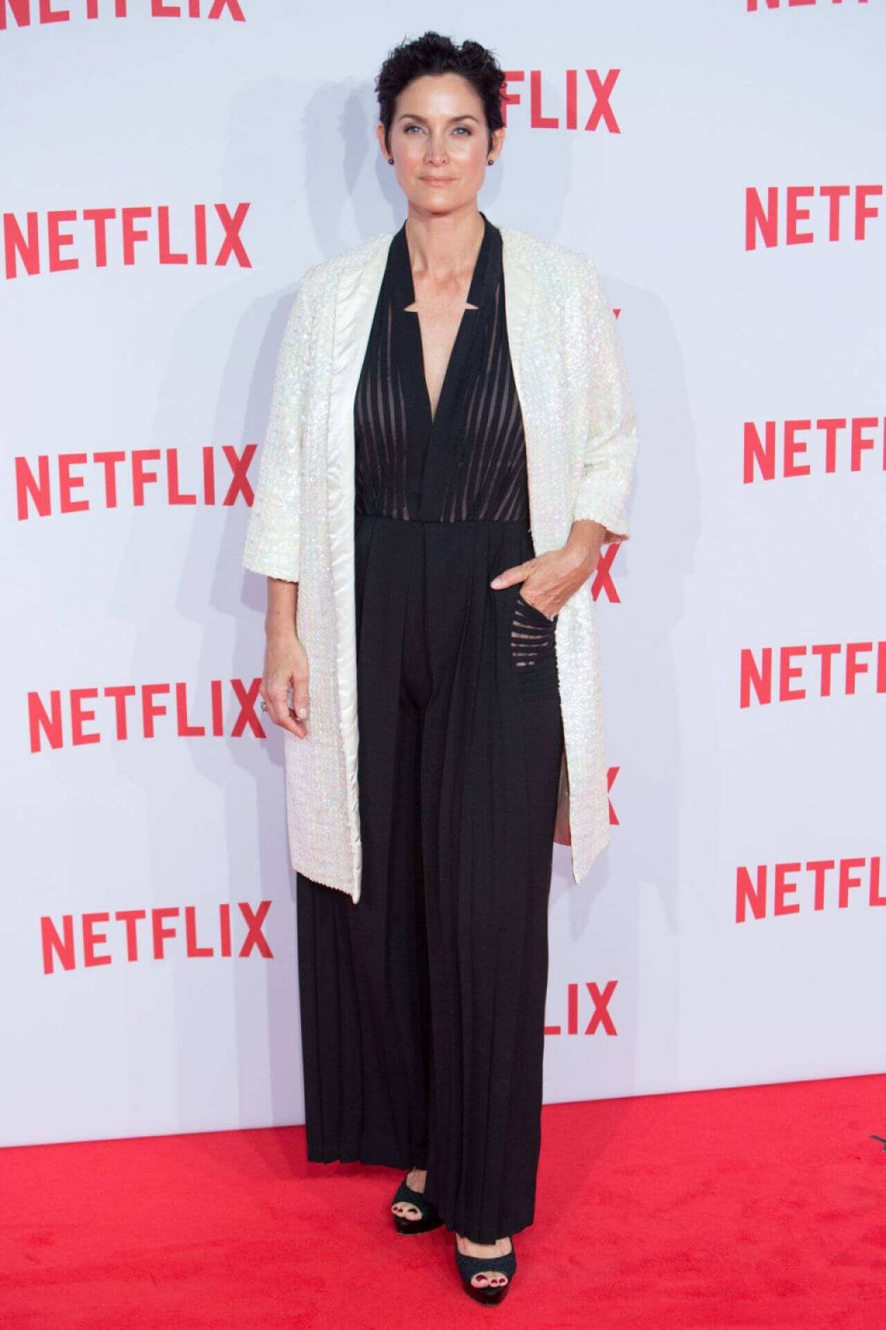 Carrie-Anne Moss  In Black Flare Jumpsuit With White Long Shrug At Netflix Spain’s Presentation Red Carpet in Madrid
